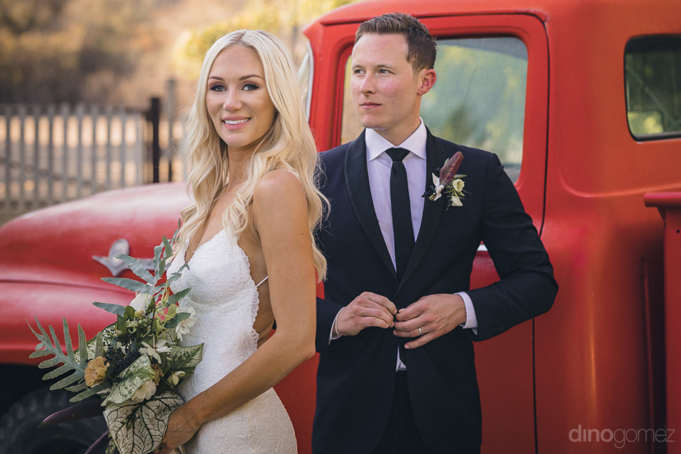 handsome groom pretty bride stand in front of old red pickup tru